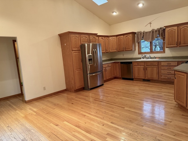 kitchen featuring high vaulted ceiling, a skylight, appliances with stainless steel finishes, and light hardwood / wood-style flooring