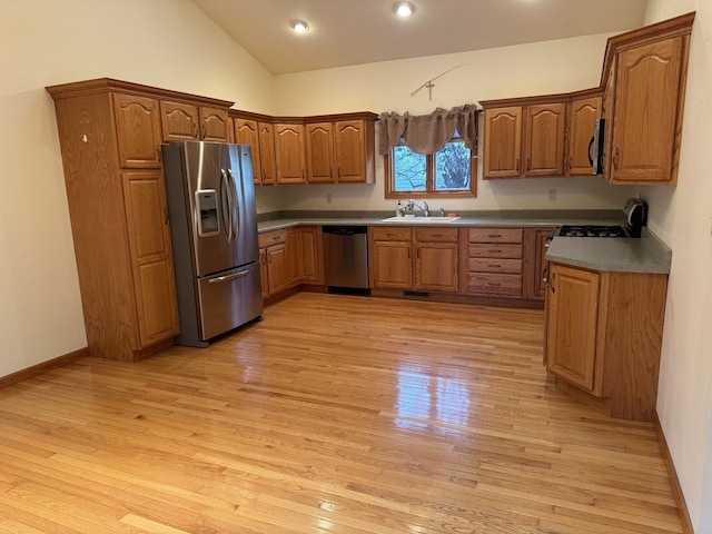 kitchen with vaulted ceiling, sink, appliances with stainless steel finishes, and light hardwood / wood-style flooring