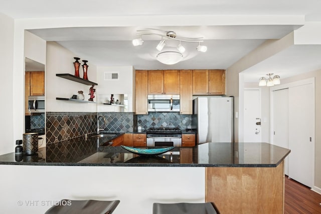 kitchen featuring visible vents, a sink, stainless steel appliances, dark stone counters, and a peninsula