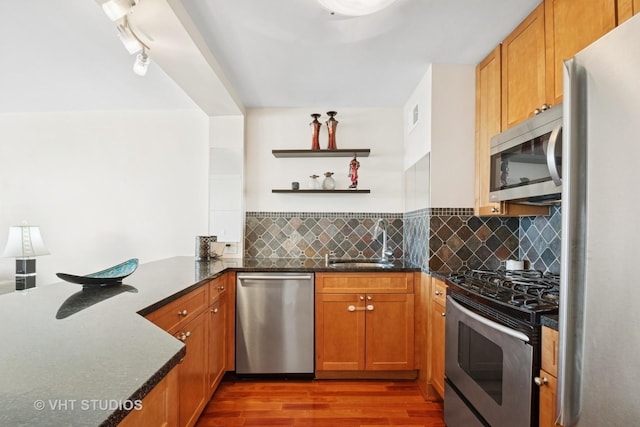 kitchen with a sink, open shelves, backsplash, wood finished floors, and appliances with stainless steel finishes