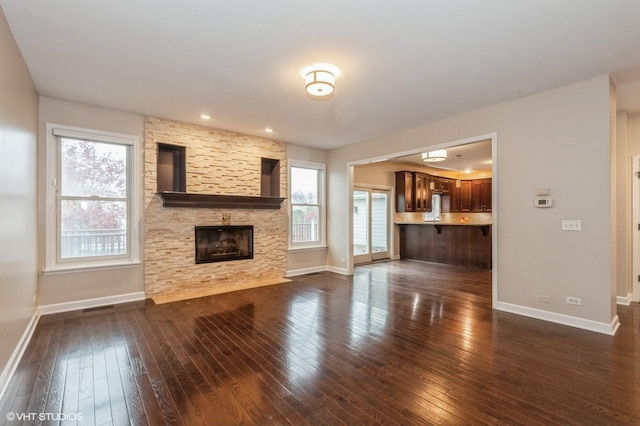 unfurnished living room with dark wood-type flooring and a stone fireplace