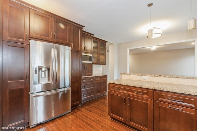 kitchen featuring dark wood-type flooring, stainless steel appliances, light stone counters, and decorative light fixtures