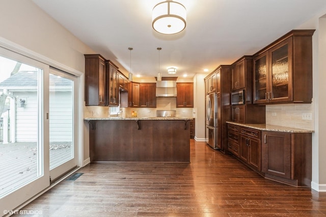 kitchen with backsplash, pendant lighting, kitchen peninsula, stainless steel appliances, and wall chimney exhaust hood