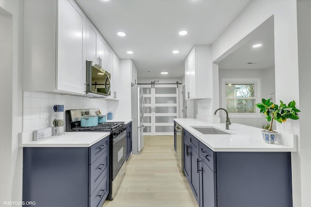 kitchen featuring stainless steel appliances, sink, a barn door, white cabinets, and light hardwood / wood-style floors