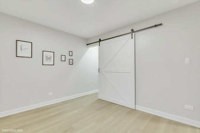 unfurnished bedroom featuring a barn door and light hardwood / wood-style floors