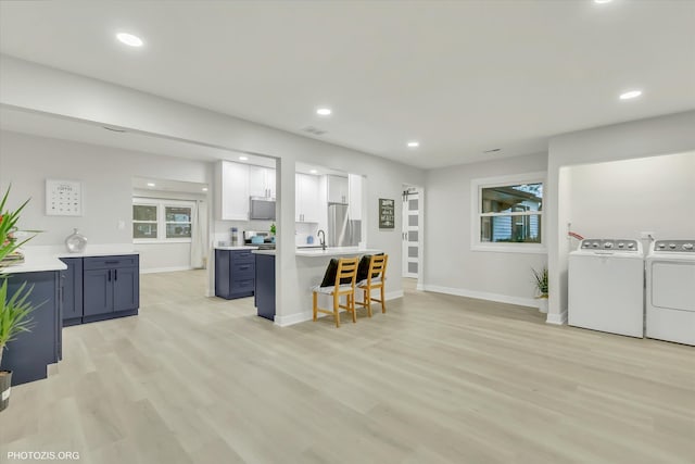 kitchen featuring washer and clothes dryer, white cabinets, a kitchen breakfast bar, blue cabinets, and light hardwood / wood-style floors