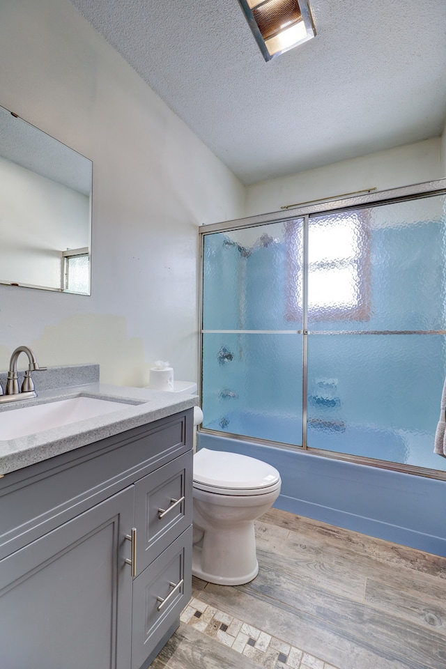 full bathroom with vanity, shower / bath combination with glass door, toilet, a textured ceiling, and wood-type flooring