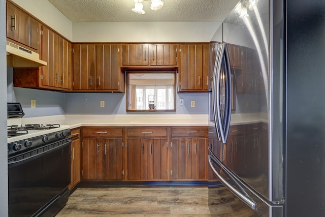 kitchen with gas stove, stainless steel fridge, wood-type flooring, and a textured ceiling