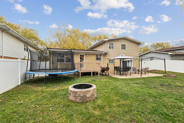 back of property with a fire pit, a lawn, a trampoline, a patio area, and a deck