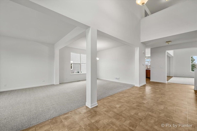 unfurnished living room featuring a towering ceiling and light colored carpet