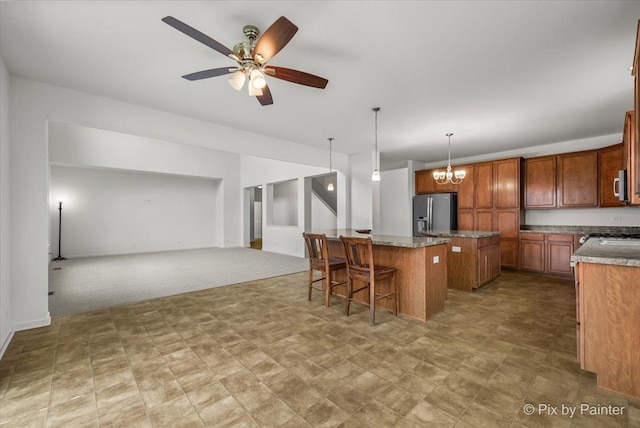 kitchen with a breakfast bar, ceiling fan with notable chandelier, stainless steel appliances, a center island, and hanging light fixtures