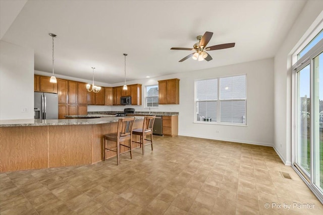 kitchen featuring a wealth of natural light, a kitchen bar, light stone countertops, and appliances with stainless steel finishes