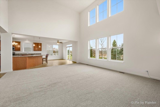 unfurnished living room featuring a high ceiling, ceiling fan with notable chandelier, light colored carpet, and sink