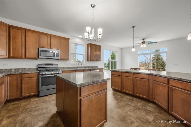 kitchen featuring pendant lighting, ceiling fan with notable chandelier, sink, a kitchen island, and stainless steel appliances