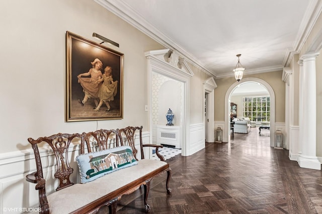 hall featuring arched walkways, wainscoting, crown molding, and ornate columns