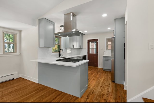 kitchen with kitchen peninsula, gray cabinetry, island range hood, sink, and light hardwood / wood-style flooring