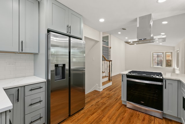 kitchen with extractor fan, gray cabinets, decorative backsplash, appliances with stainless steel finishes, and light wood-type flooring