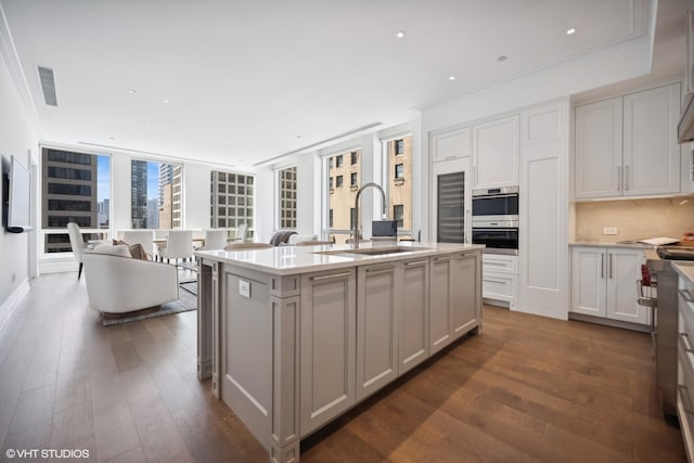 kitchen with a kitchen island with sink, white cabinets, sink, dark hardwood / wood-style floors, and decorative backsplash