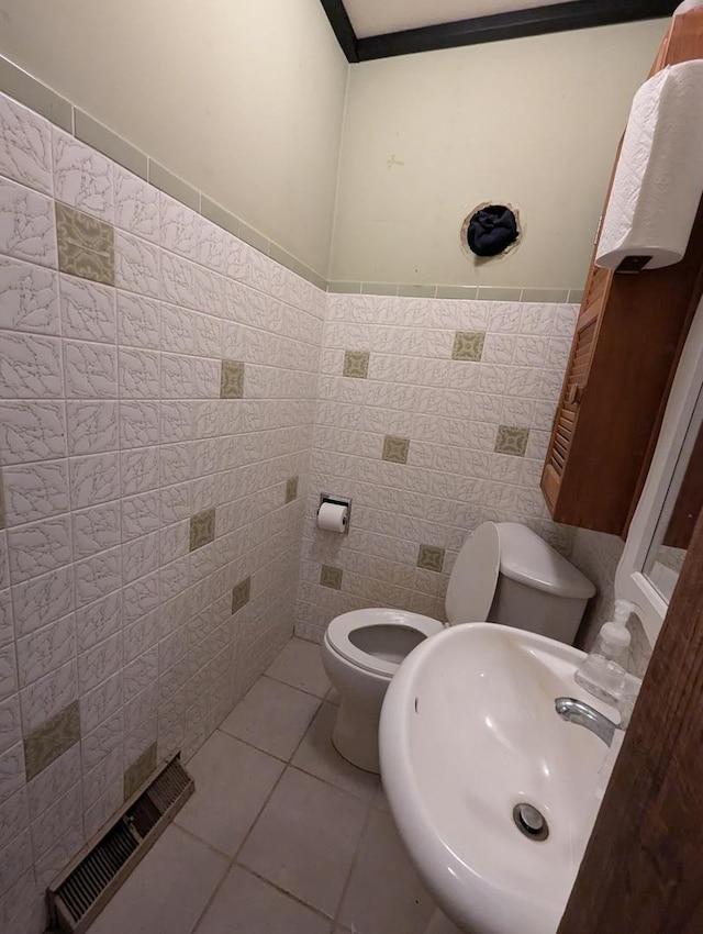 half bath with toilet, a sink, tile patterned floors, tile walls, and wainscoting