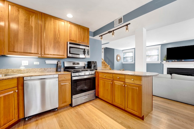 kitchen with rail lighting, sink, light hardwood / wood-style floors, kitchen peninsula, and stainless steel appliances