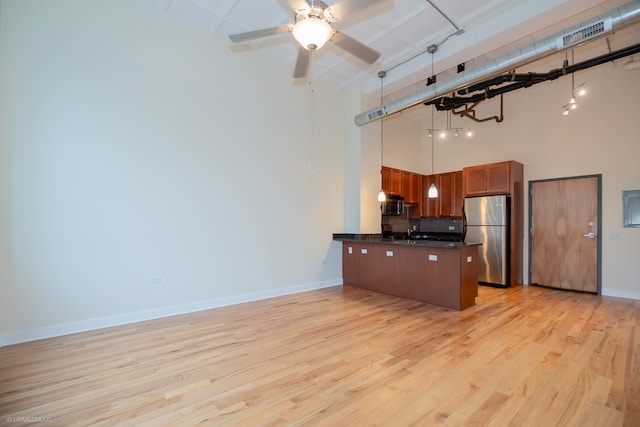 kitchen featuring hanging light fixtures, light wood-type flooring, a high ceiling, and stainless steel refrigerator