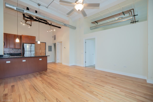 kitchen with pendant lighting, a high ceiling, decorative backsplash, stainless steel fridge, and light wood-type flooring