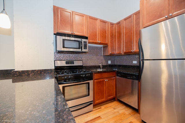 kitchen with dark stone countertops, pendant lighting, stainless steel appliances, and light wood-type flooring