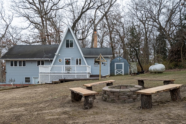 rear view of property featuring a shed, a deck, and an outdoor fire pit