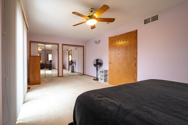 bedroom featuring light carpet, ceiling fan, and multiple closets