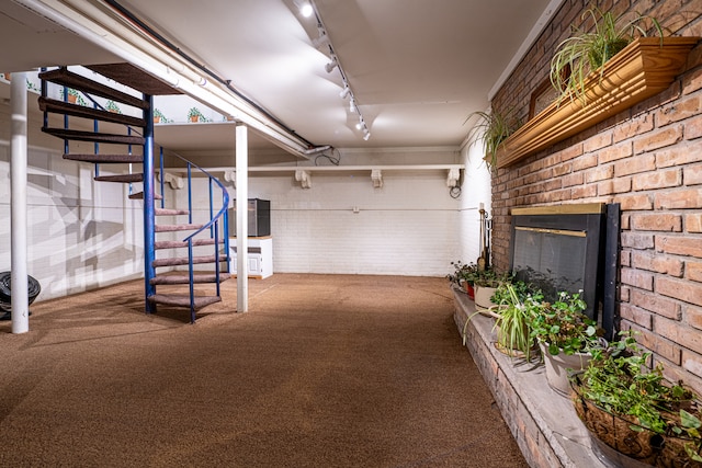 basement featuring carpet flooring, track lighting, a brick fireplace, and brick wall