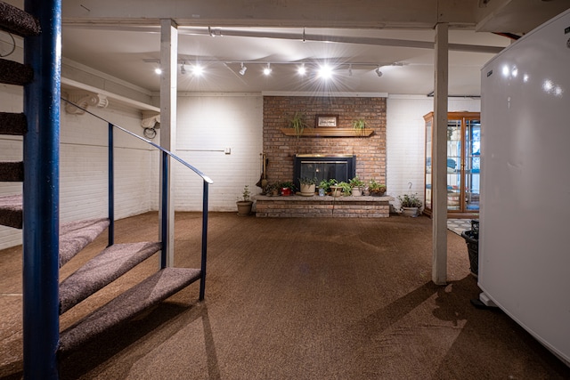 basement with carpet flooring, rail lighting, a brick fireplace, and brick wall