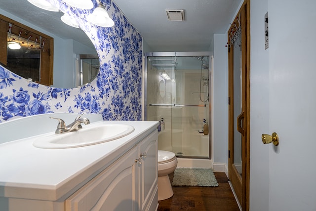 bathroom featuring vanity, a textured ceiling, wood-type flooring, toilet, and a shower with shower door