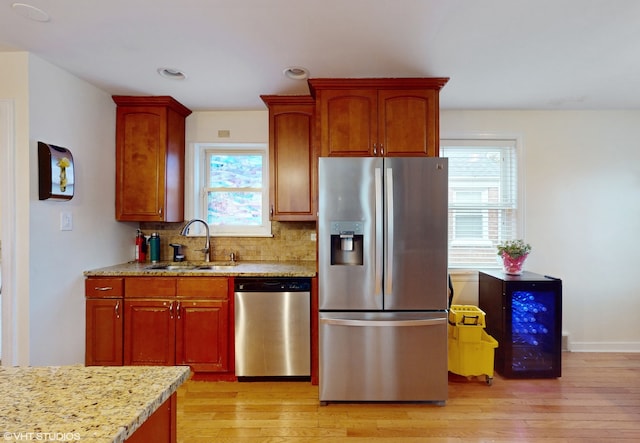 kitchen featuring decorative backsplash, appliances with stainless steel finishes, light stone counters, sink, and light hardwood / wood-style flooring