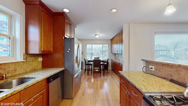 kitchen with appliances with stainless steel finishes, light wood-type flooring, backsplash, light stone counters, and pendant lighting