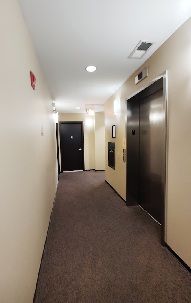 hall with dark colored carpet and elevator