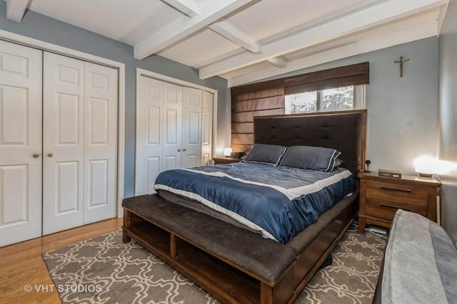 bedroom featuring two closets, wood-type flooring, and beam ceiling