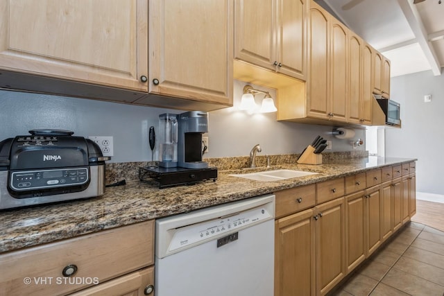 kitchen featuring dark stone countertops, light brown cabinetry, sink, white dishwasher, and light tile patterned floors