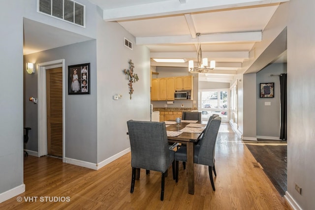 dining area featuring light wood-type flooring, a notable chandelier, and beamed ceiling