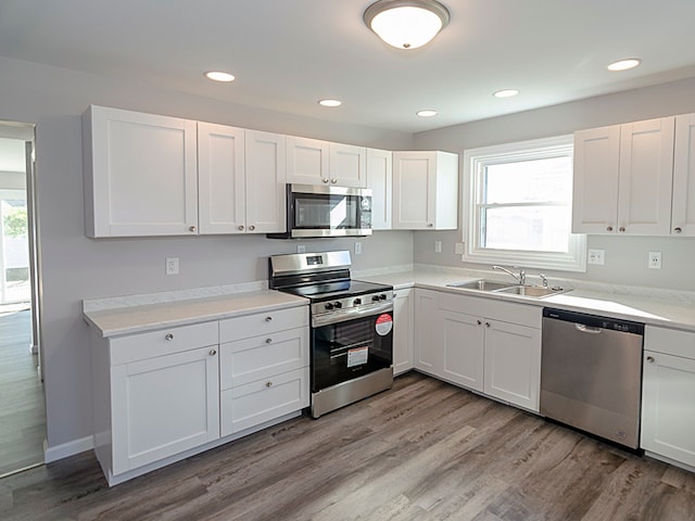 kitchen with white cabinets, light wood-type flooring, stainless steel appliances, and sink