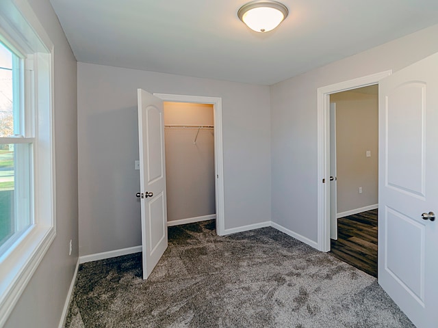 unfurnished bedroom featuring a spacious closet, a closet, and dark colored carpet