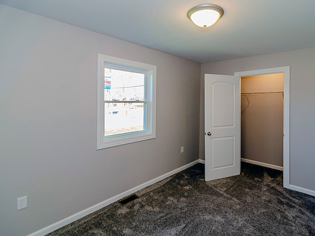 unfurnished bedroom with dark carpet, a spacious closet, and a closet