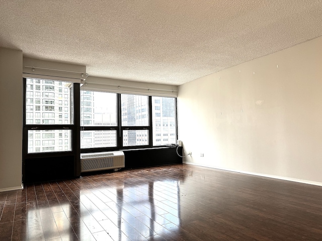 empty room with a textured ceiling, dark hardwood / wood-style floors, and a wall unit AC