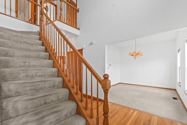 staircase with visible vents, a towering ceiling, wood finished floors, a chandelier, and baseboards