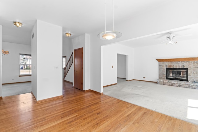 unfurnished living room with light wood-style flooring, a brick fireplace, stairway, and baseboards