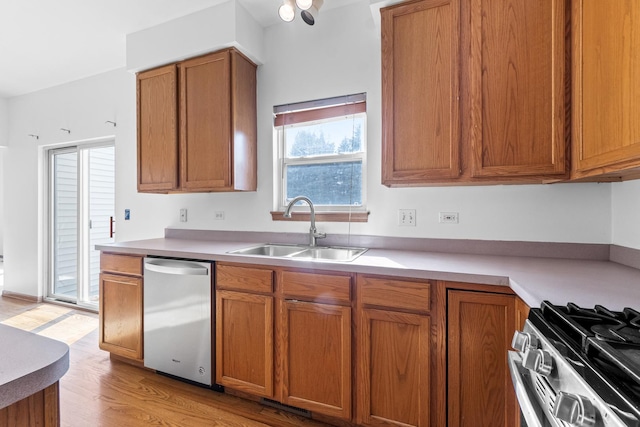 kitchen featuring light wood finished floors, brown cabinets, stainless steel appliances, light countertops, and a sink