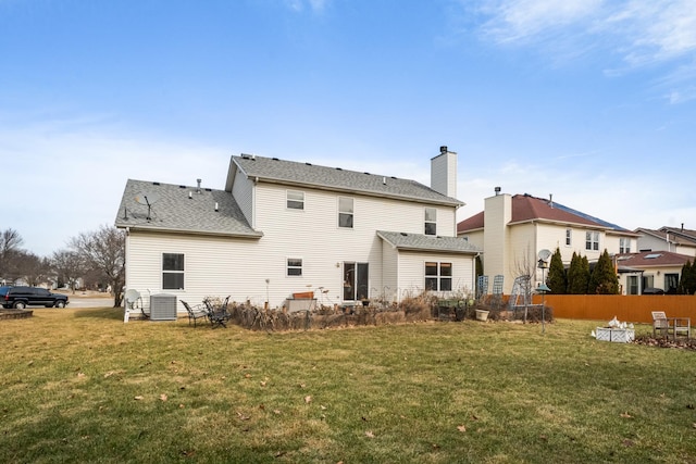 rear view of house featuring roof with shingles, fence, and a yard