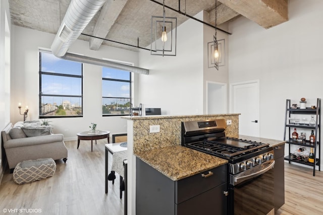 kitchen with light wood finished floors, light stone counters, open floor plan, a high ceiling, and stainless steel range with gas stovetop