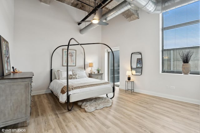 bedroom featuring a high ceiling, wood finished floors, a ceiling fan, and baseboards