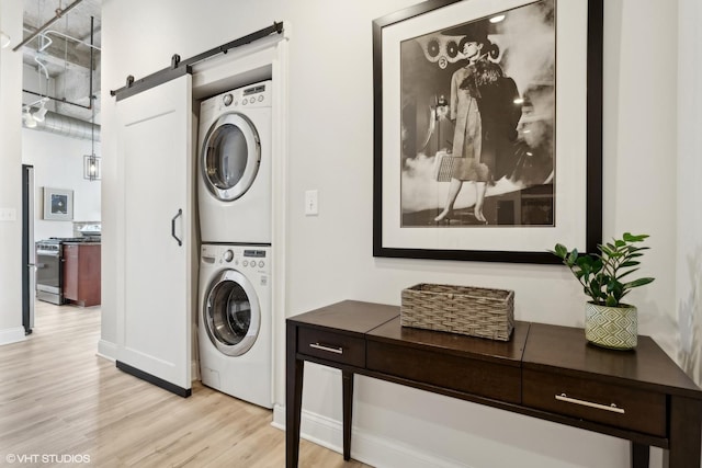 laundry room featuring stacked washer / dryer, laundry area, light wood finished floors, and a barn door