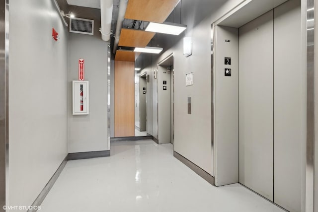 hallway featuring concrete flooring, elevator, and visible vents